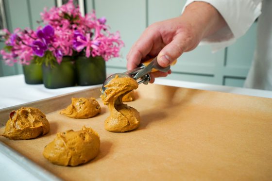 A person scooping cookie dough onto a baking pan.